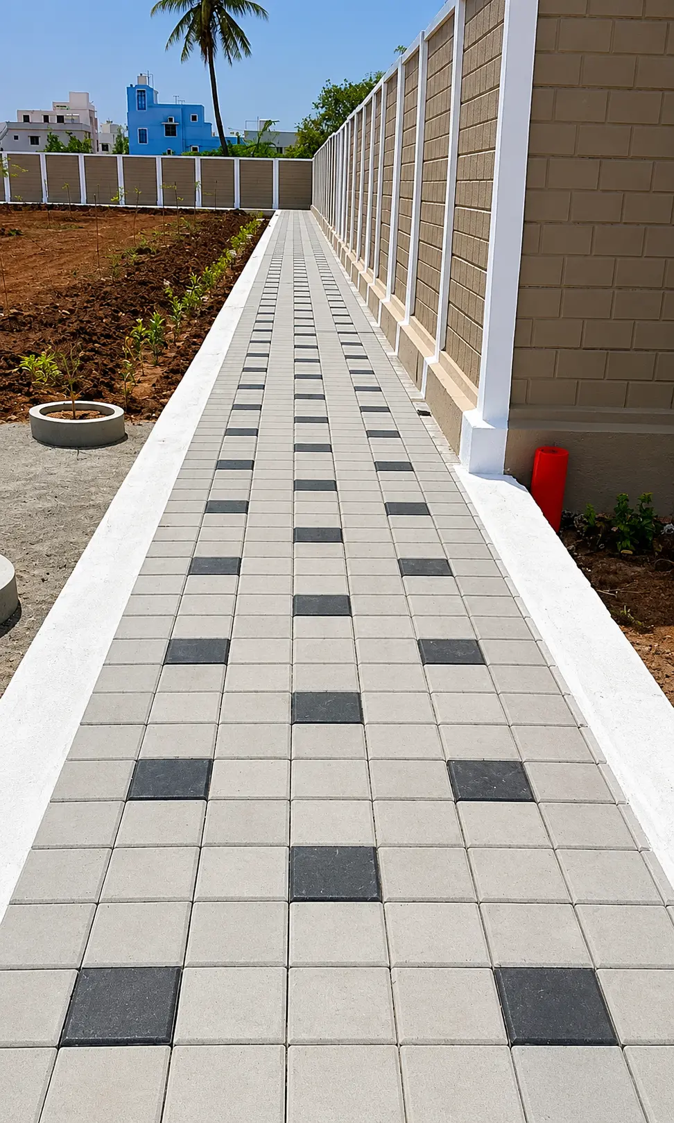 Long walkway of grey square pavers with black square accents beside a compound wall